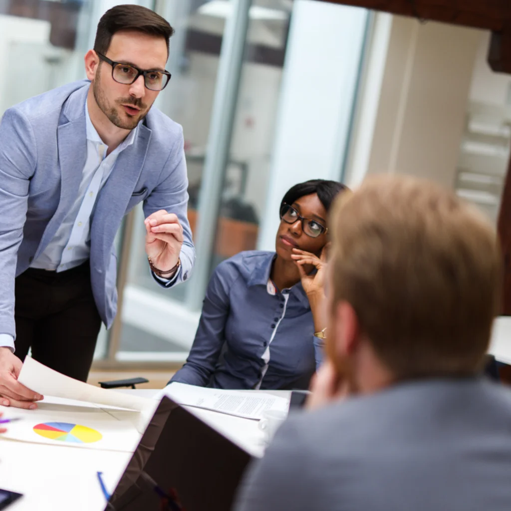 Ein HR Manager steht in einem Büro mit zwei weiteren Mitarbeitenden 