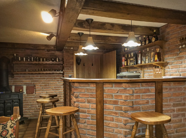 Fotografie eine Kellerbar mit einer Bar aus Backstein und Holz mit mehreren Barhockern aus Holz und haengenden Lampen